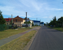 Zdjęcie przedstawia główną drogę we wsi Rusko wraz z zabudowaniami.                                                                                                                                     