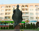 Fotografia przedstawia Pomnik Jana Pawła II na tle bloków mieszkalnych                                                                                                                                  