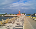 Zdjęcie przedstawia falochron w Darłówku Wschodnim - nadmorskiej dzielnicy Darłowa z widokiem na latarnię morską.                                                                                       