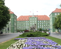 Zdjęcie przedstawia budynki urzędu miasta Szczecin wraz z pomnikiem Gryfa i kwietnikiem.                                                                                                                