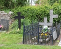 Zdjęcie przedstawia cmentarz przykościelny w Sobieradzu. Na pierwszym planie widać trzy żeliwne krzyże - jeden z nich ma połamane ramię.                                                                