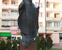 Fotografia przedstawia |Pomnik Jana Pawła II na tle bloków mieszkalnych .                                                                                                                               