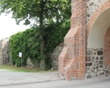 Zdjęcie przedstawia obwarowania miejskie w Trzcińsku-Zdroju. Na pierwszym planie widać mur i fragment bramy.                                                                                            