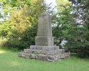 Zdjęcie przedstawia pomnik poświęcony ofiarom I wojny światowej. Na pierwszym planie widać obelisk na tle drzew.                                                                                        