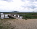 Zdjęcie przedstawia plażę nad jeziorem Łętowskim z pomostem.                                                                                                                                            