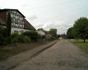 Zdjęcie przedstawia drogę we wsi Żukowo wraz zabudowaniami.                                                                                                                                             