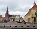 Zdjęcie przedstawia Ratusz, plac oraz budynki sąsiadujące które znajdują się na Terenie Starego Miasta oraz kościół w oddali                                                                            