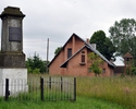 Zdjęcie przedstawia kamienny pomnik otoczony niskim ogrodzeniem oraz kościół w tle.                                                                                                                     