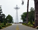 Zdjęcie przedstawia szerokie ujęcie barwnych ogrodów otaczających krzyż, znajdujący się w jego centrum                                                                                                  