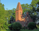 Zdjęcie przedstawia kościół w Jastrzębnikach w otoczeniu ozdobnych krzewów i drzew.                                                                                                                     