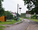 Zdjęcie przedstawia brukowaną uliczkę, przystanek autobusowy oraz zamieszkane bocianie gniazdo                                                                                                          