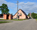 Zdjęcie przedstawia jedną z ulic w Łopianowie wraz z przystankiem autobusowym oraz budynkami sąsiadującymi                                                                                              