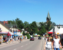 Zdjęcie przedstawia zatłoczoną ulicę w Ustroniu Morskim. Po bokach kawiarnie i sklepy z pamiątkami.                                                                                                     