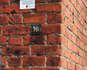 Zdjęcie przedstawia oznakowanie szlaku na murze z czerwonej cegły                                                                                                                                       