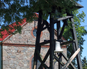 Zdjęcie przedstawia front kościoła w Rusinowie, na pierwszym planie drewniana dzwonnica.                                                                                                                