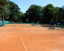 Widok na pomarańczowy kort tenisowy wraz z ogrodzeniem                                                                                                                                                  