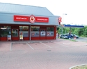 Zdjęcie przedstawia sklep Małpka Express wraz z przylegającym do niego parkingiem dla klientów.                                                                                                         