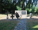 Zdjęcie przedstawia tablicę i krzyże pamiątkowe na cmentarzu przykościelnym.                                                                                                                            