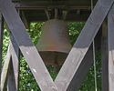 Zdjęcie przedstawia zbliżenie dzwonu zawieszonego na drewnianej dzwonnicy przy kościele w Czarnkowiu.                                                                                                   