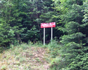 Zdjęcie przedstawia część lasu oraz tablicę informacyjną w Rezerwacie Przyrody Brunatna Gleba.                                                                                                          