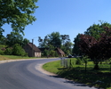 Zdjęcie przedstawia główną drogę we wsi Wszedzień wraz  z zabudowaniami.                                                                                                                                