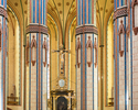 Widok na wnętrze kościoła, widoczne są zdobione kolumny, a po środku widoczny jest krzyż znajdujący się na szczycie ołtarza                                                                             