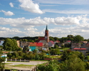 Zdjęcie przedstawia panoramę miasta z wyraźnie widoczną wieżą kościelną kościoła parafialnego pw. Niepokalanego Poczęcia NMP w Resku.                                                                   